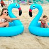 Due bambine giocano sulla spiaggia con gonfiabili a forma di fenicottero blu.