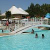 Piscina con un piccolo ponte bianco, bagnanti e ombrelloni, con un grande gazebo sullo sfondo.