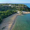 Una spiaggia con ombrelloni e lettini vicino a una collina verde.