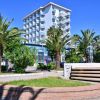 Alta palazzina moderna con balconi, circondata da palme e un'aiuola con una statua.