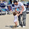 Un adulto gioca con un bambino sulla spiaggia vicino a lettini e ombrelloni.