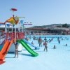 Piscina affollata con scivoli colorati e aree giochi.