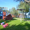 Parco giochi colorato su prato verde, con scivoli e strutture per arrampicarsi tra gli alberi.