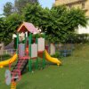 Parco giochi con scivolo giallo, altalene e casetta su prato verde.