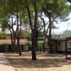 Piccole case tra alberi in un campeggio, con sentieri di mattoni e prati.