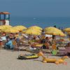 Spiaggia affollata con lettini e ombrelloni gialli vicino al mare.