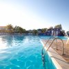 Piscina con scivolo colorato, ombrelloni e riflessi del sole sull'acqua.