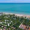 Vista aerea di un litorale con mare blu, spiaggia attrezzata e complesso turistico verde.