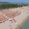 Ampia spiaggia affollata con file di ombrelloni e sdraio, vista dall'alto.