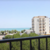 Vista su edifici alti, alberi e mare in lontananza, osservata da un balcone.