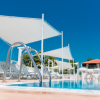 Piscina blu con sedie a sdraio e vele bianche sotto un cielo azzurro.