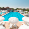 Ampia piscina blu con ombrelloni bianchi e lettini intorno, cielo sereno.