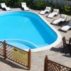 Piscina ovale circondata da lettini bianchi, con tavolo e sedie a lato.