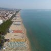 Spiaggia lunga con ombrelloni colorati e città sullo sfondo.