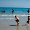 Bambini giocano al mare mentre adulti nuotano nelle vicinanze.