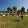Persone fanno esercizi di yoga su un prato vicino al mare sotto un cielo azzurro.